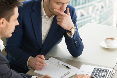 Business partners using laptop while working together on important corporate project in office. Businessman attentively listening to adviser Investment specialist making presentation of promising deal